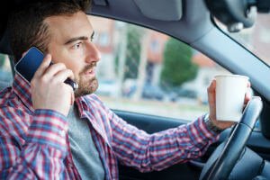 man talking on phone and drinking beverage while driving