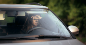woman in car with hands over eyes