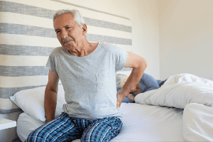 Elderly man holding his back in pain as he gets out of bed