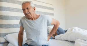 Elderly man holding his back in pain as he gets out of bed