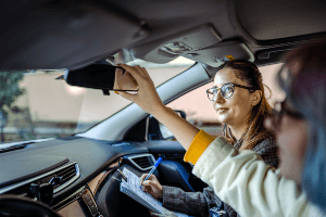 Driving instructor taking notes while student driver checks the rearview mirror.