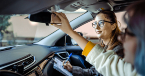 Driving instructor taking notes while student driver checks the rearview mirror.
