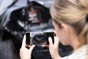 young blonde woman taking a cellphone pic of vehicle damage