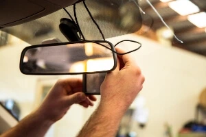 A person setting up a dashcam behind the mirror of their car.
