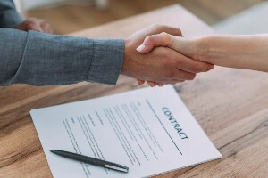 Two people shaking hands over a contract.