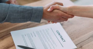 Two people shaking hands over a contract.