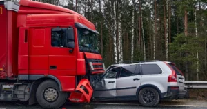 A gray car crushed under the hood of a red truck