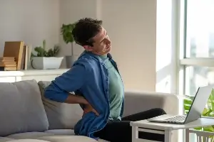 A man holding his lower back while on the couch.