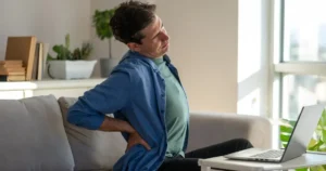 A man holding his lower back while on the couch.
