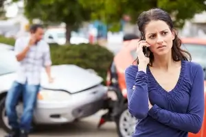 A female on the phone standing in front of a car crash.
