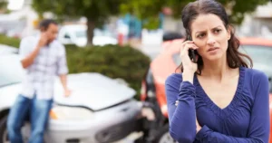 A female on the phone standing in front of a car crash.